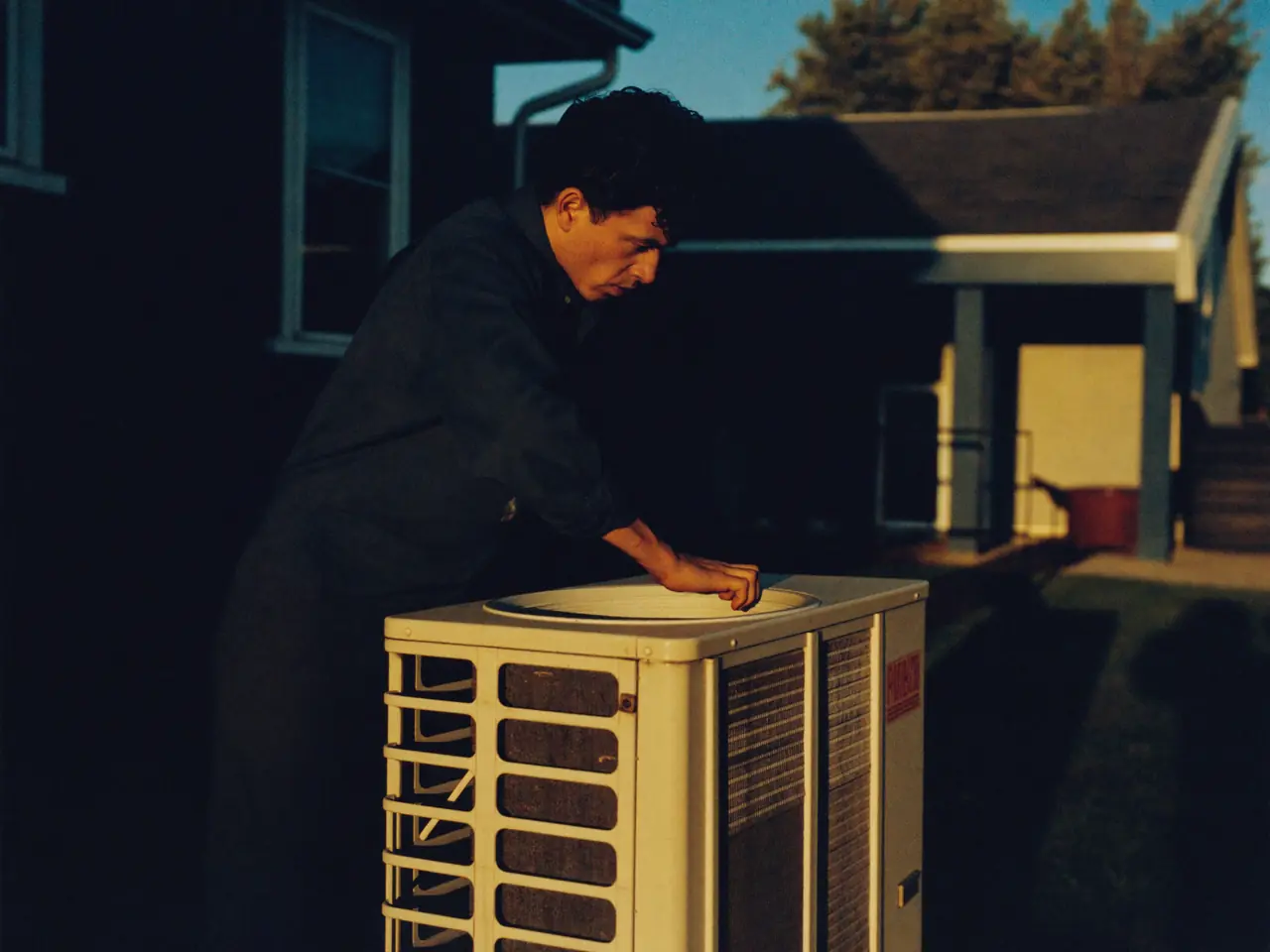 Técnico de aire acondicionado revisando la unidad exterior de una casa al atardecer